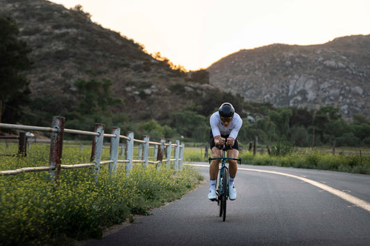Man cycling on a road next to a wooden fence with hills behind him
