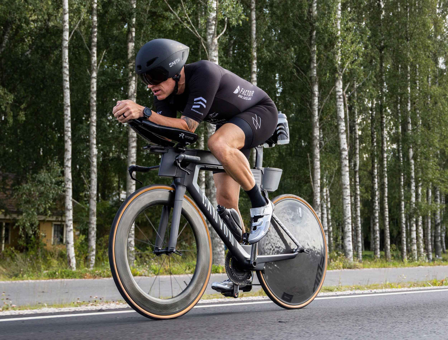 Man cycling next to skinny trees wearing Mauna suit