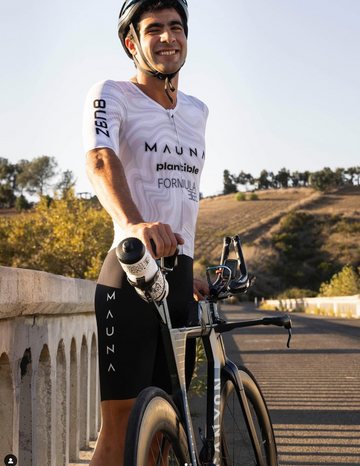 Man wearing a Mauna suit leaning on his bicycle smiling at the camera